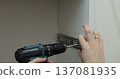Man using a electric drill to attach a metal drawer slide to a piece of furniture during assembly. Furniture installation. 137081935