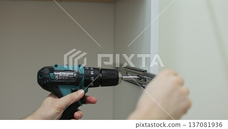 Man using a electric drill to attach a metal drawer slide to a piece of furniture during assembly. Furniture installation. 137081936