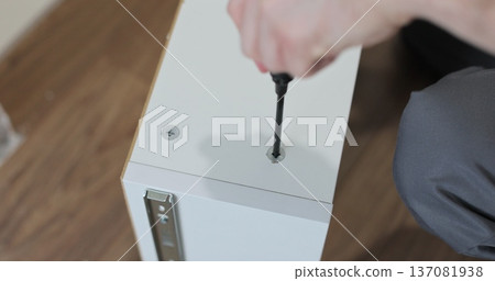 Man assembling kitchen drawer in modern cabinet using screwdriver. Furniture installation. Man assembling kitchen drawer in modern cabinet using screwdriver. Furniture installation. 137081938