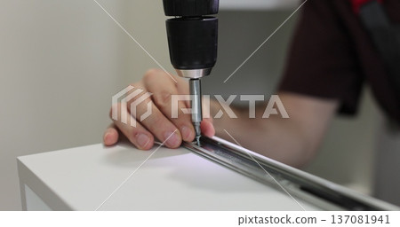 Close-up of person driving screw with cordless drill into furniture panel, assembling drawer. Close-up of person driving screw with cordless drill into furniture panel, assembling drawer. 137081941