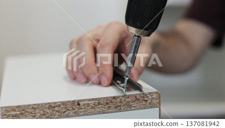 Man using a electric drill to attach a metal drawer slide to a piece of furniture during assembly. Furniture installation. 137081942