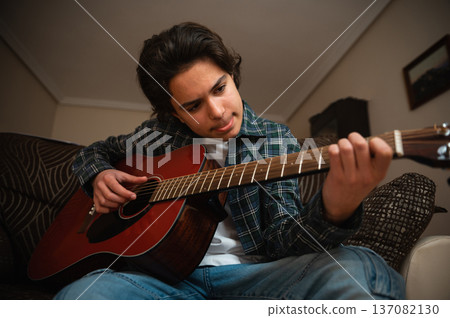 Teenage Boy Playing Acoustic Guitar at Home in Cozy Casual Setting 137082130