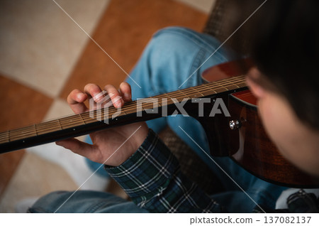 Teenage Boy Playing Acoustic Guitar at Home in Cozy Casual Setting Teenage Boy Playing Acoustic Guitar at Home in Cozy Casual Setting 137082137