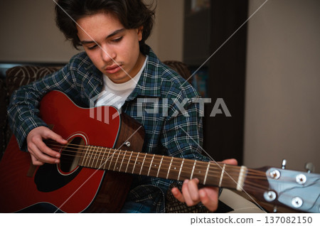 Teenage Boy Playing Acoustic Guitar At Home In Cozy Casual Setting Teenage Boy Playing Acoustic Guitar At Home In Cozy Casual Setting 137082150