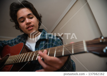 Teenage Boy Playing Acoustic Guitar at Home, Strumming and Practicing in Cozy Interior Teenage Boy Playing Acoustic Guitar at Home, Strumming and Practicing in Cozy Interior 137082162
