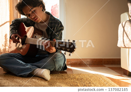 Teenage Boy Playing Acoustic Guitar At Home Sitting On Floor In Cozy Sunlit Room Teenage Boy Playing Acoustic Guitar At Home Sitting On Floor In Cozy Sunlit Room 137082185