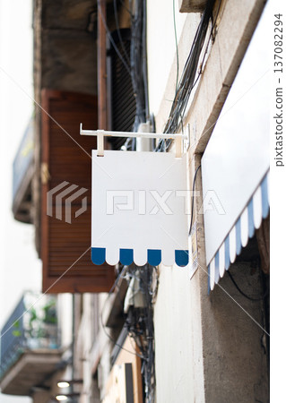 Blank rectangular shop sign blue scalloped edges hanging from a metal bracket 137082294