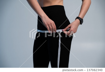 Woman measuring hips with a tape to track weight loss, body transformation 137082340
