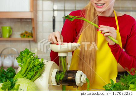 Woman in kitchen making vegetable smoothie juice Woman in kitchen making vegetable smoothie juice 137083285
