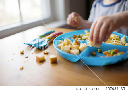 Little child eating healthy food from a blue plate on a wooden table 137083485