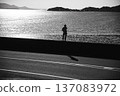 逆光照射下的水面和站在沙灘上的人的剪影（單色） 137083972