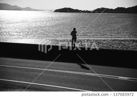 Backlit water surface and silhouette of a person standing on the beach (monochrome) Backlit water surface and silhouette of a person standing on the beach (monochrome) 137083972