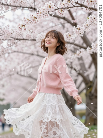 Beautiful young Asian woman smiling under blooming cherry blossom trees, wearing pink cardigan and white lace skirt, spring fashion and hanami concept. 137084701