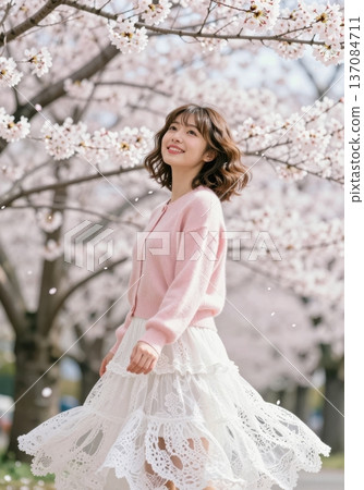 Beautiful young Asian woman smiling under blooming cherry blossom trees, wearing pink cardigan and white lace skirt, spring fashion and hanami concept. 137084711