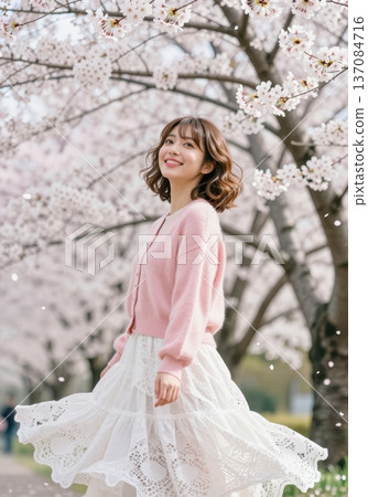 Beautiful young Asian woman smiling under blooming cherry blossom trees, wearing pink cardigan and white lace skirt, spring fashion and hanami concept. 137084716