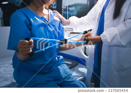Physical therapist giving stretching exercises with elastic exercise bands and physical therapist hands helping male patient Physical therapy concept Physical therapist giving stretching exercises with elastic exercise bands and physical therapist hands helping male patient Physical therapy concept 137085454