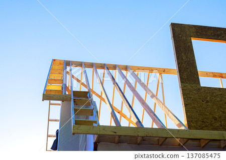 Workers build framework of wooden building with beam roof trusses at construction site Workers build framework of wooden building with beam roof trusses at construction site 137085475