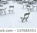 A minimalist winter scene showing empty outdoor cafe chairs and tables scattered across a snow-covered terrace 137085551
