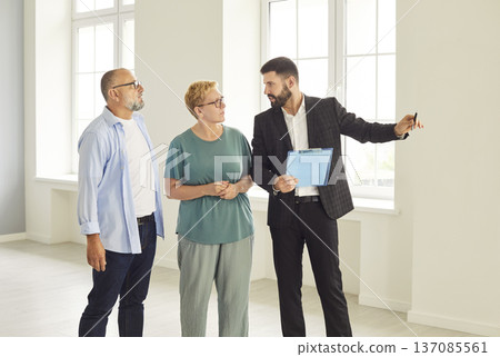 Realtor showing bright modern apartment interior to mature couple during tour 137085561