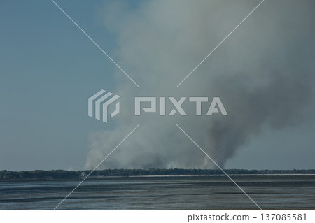 A distant wildfire sends a towering column of smoke into the sky above a small coastal island near Vlora, Albania, captured on August 25, 2025.  137085581