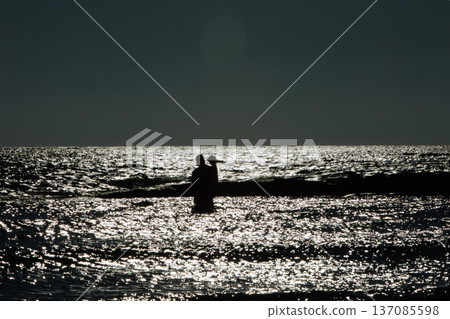 Silhouette of an adult with a child standing in shallow water at sunset in Vlora, Albania, captured on August 25, 2025. The sparkling sea reflects the fading light Silhouette of an adult with a child standing in shallow water at sunset in Vlora, Albania, captured on August 25, 2025. The sparkling sea reflects the fading light 137085598