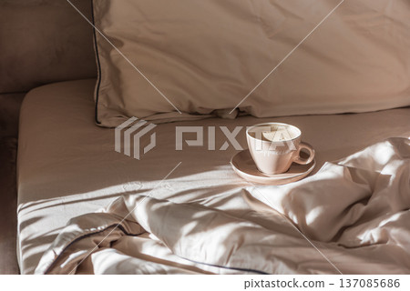 Cappuccino Cup on Cozy Bed with Sunlight and Beige Bedding Cappuccino Cup on Cozy Bed with Sunlight and Beige Bedding 137085686