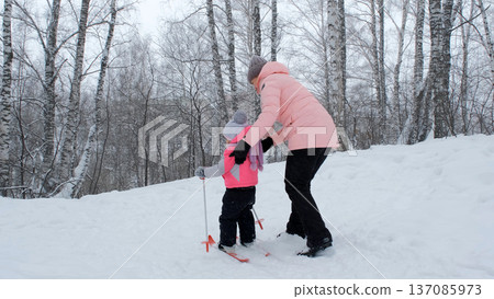 A cute girl learns skiing with her mother on a snowy day while exploring winter fun together 137085973