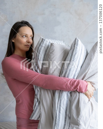 woman holds pile of pillows in her hands. pillows are in different colors, look like stack. woman holds pile of pillows in her hands. pillows are in different colors, look like stack. 137086120