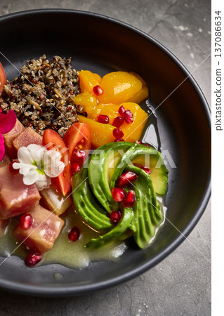 Colorful bowl with quinoa, avocado, tuna, cherry tomatoes, pomegranate seeds, peaches, flower garnish, superfood mix, vibrant presentation, healthy eating concept 137086634