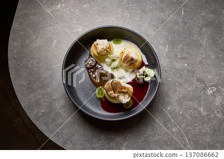 Elegant dessert with meringue, grapes, cream, garnished with flower on black plate over marble table culinary art concept 137086662