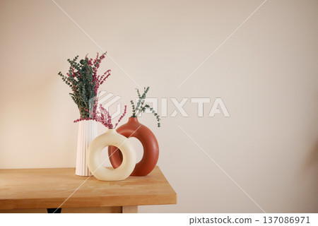 Vases with flowers on wooden table in simple room 137086971