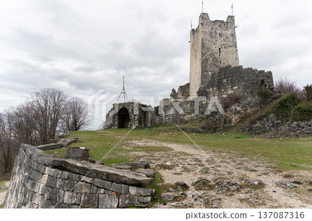 Anakopia fortress tower and stone walls on grassy hilltop under cloudy sky in Abkhazia. Image supports heritage tourism marketing, historical education projects and travel destination Anakopia fortress tower and stone walls on grassy hilltop under cloudy sky in Abkhazia. Image supports heritage tourism marketing, historical education projects and travel destination 137087316