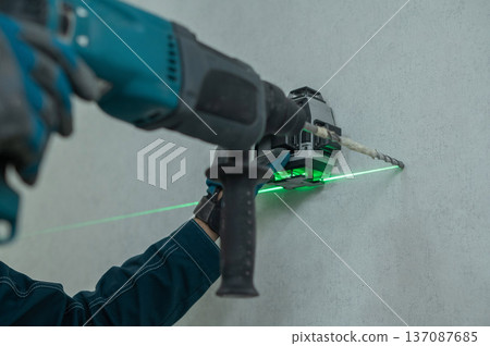 A man measures distances with a laser level and drills into a wall with a hammer drill. A man measures distances with a laser level and drills into a wall with a hammer drill. 137087685