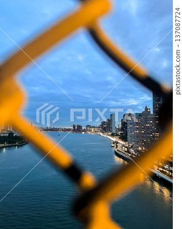 Dusk settles on the East River in New York City, with Manhattan on the right, Roosevelt Island ahead, winter tones on water and sky, and fence bokeh framing the scene. Dusk settles on the East River in New York City, with Manhattan on the right, Roosevelt Island ahead, winter tones on water and sky, and fence bokeh framing the scene. 137087724