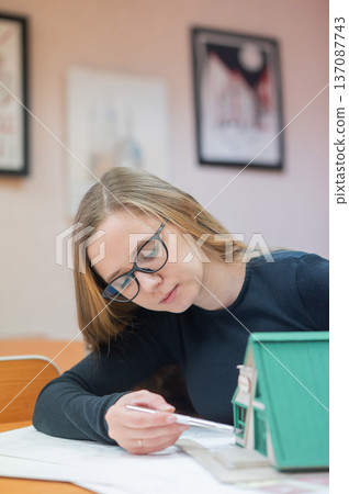 Caucasian young woman making a model of a building. Student of the construction university. Caucasian young woman making a model of a building. Student of the construction university. 137087743