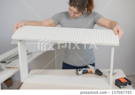 A Caucasian woman assembles furniture. A Caucasian woman assembles furniture. 137087785