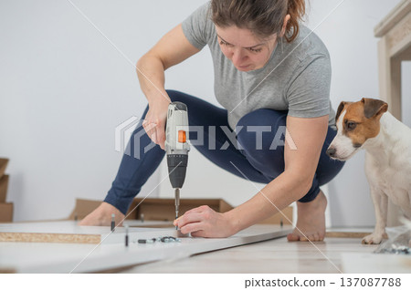 A Caucasian woman uses a screwdriver to tighten a screw while assembling a cabinet. 137087788