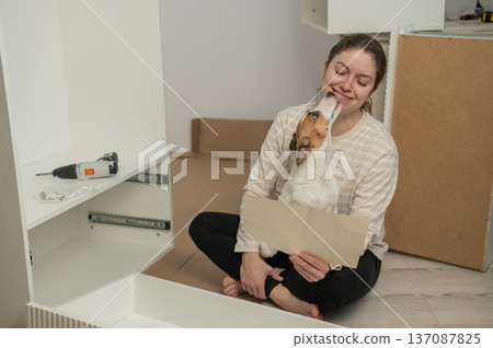 A Caucasian woman assembles furniture with her cute dog. A Caucasian woman assembles furniture with her cute dog. 137087825