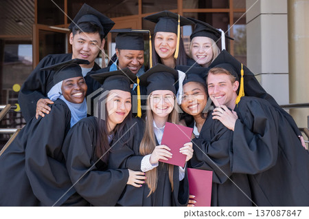 Happy students of different nationalities in graduation gowns hold their diplomas. Happy students of different nationalities in graduation gowns hold their diplomas. 137087847
