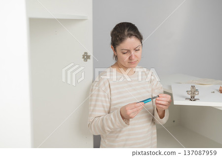 A Caucasian woman assembles a wardrobe. She understands the hardware. A Caucasian woman assembles a wardrobe. She understands the hardware. 137087959
