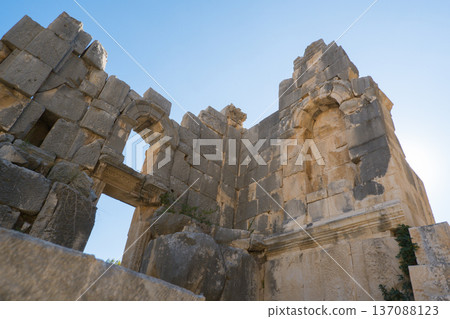 A stunning view of ancient stone ruins featuring a grand archway, framed by towering stone blocks and set against a vibrant blue sky. This historic site in Demre, Turkey 137088123