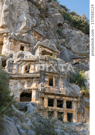 A breathtaking view of ancient Lycian rock-cut tombs embedded in a rugged cliffside in Demre, Turkey. The historic tombs showcase intricate stone architecture, blending seamlessly with the natural 137088124