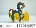 A gold and blue horse figurine is sitting on a white plate with two yellow rocks 137089057