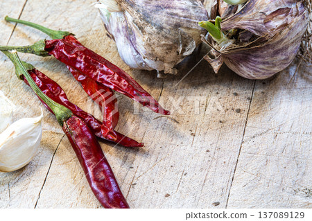 A bunch of red peppers and garlic on a wooden table. The peppers are dried and the garlic is fresh 137089129