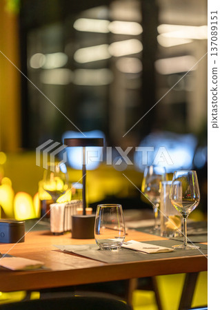 Tables are set with glasses and napkins in a well-designed restaurant. Guests dine and socialize under soft lighting in a lively atmosphere during the evening. Tables are set with glasses and napkins in a well-designed restaurant. Guests dine and socialize under soft lighting in a lively atmosphere during the evening. 137089151