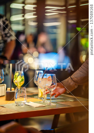 Guests sit at a table with drinks in hand while others engage in conversation at a restaurant. The atmosphere is busy and filled with laughter and chatter. 137089168