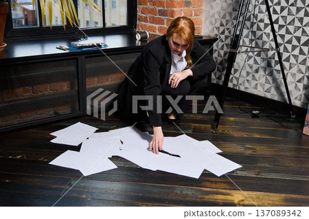 Woman with fiery hair arranging scattered designs urgently 137089342
