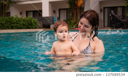 Caucasian woman holds her son while swimming in a pool on vacation. Mom teaches little boy to swim.  137089534