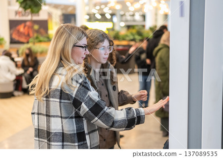 A mother and her teenage daughter are walking through a shopping mall. A mother and her teenage daughter are walking through a shopping mall. 137089535