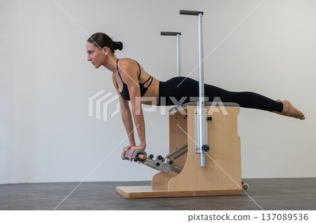 Caucasian woman doing Pilates on classic chair. Caucasian woman doing Pilates on classic chair. 137089536